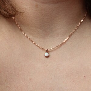 May include: A delicate rose gold chain necklace with a small white opal pendant.