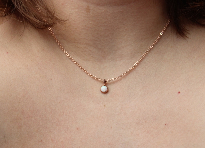 May include: A delicate rose gold chain necklace with a small white opal pendant.