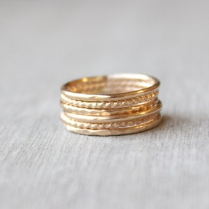 May include: A set of six gold stacking rings with different textures, including hammered, twisted, and smooth.