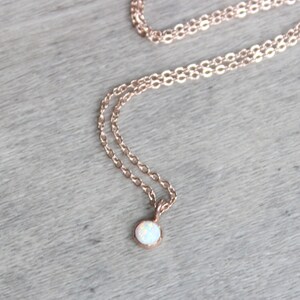 May include: A delicate rose gold chain necklace with a small, round white opal pendant.