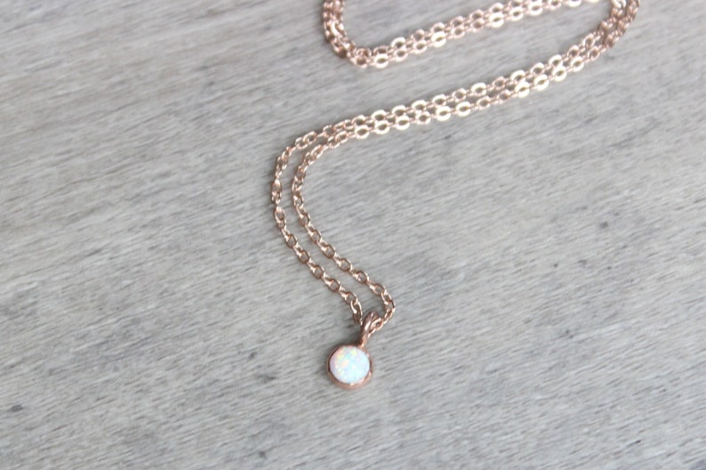 May include: A delicate rose gold chain necklace with a small, round white opal pendant.