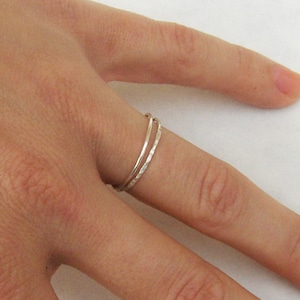 May include: Two thin silver rings worn on a finger. The rings are simple and delicate, with a hammered texture.