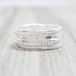 May include: A silver ring featuring multiple bands, each with a distinct texture. The bands are layered on top of one another, resulting in a unique and stylish design.
