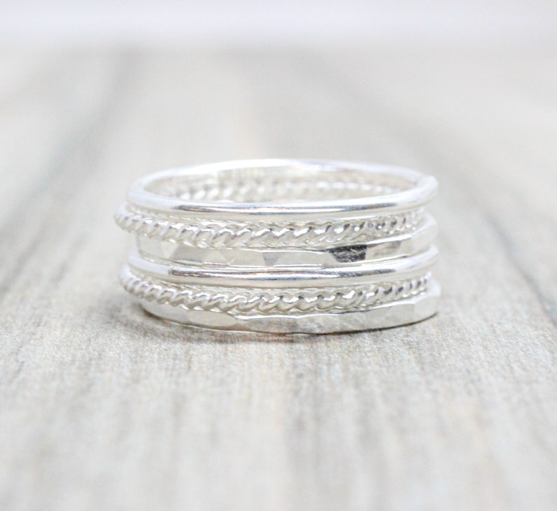 May include: A silver ring featuring multiple bands, each with a distinct texture. The bands are layered on top of one another, resulting in a unique and stylish design.