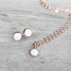 May include: A set of rose gold jewelry featuring a delicate chain necklace and matching stud earrings. Each piece is adorned with a small, round white opal.