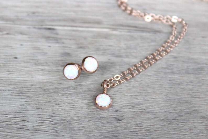 May include: A set of rose gold jewelry featuring a necklace and earrings with white opal stones.