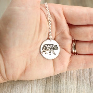 May include: Silver necklace with a round pendant featuring a bear silhouette with floral details and the word "mama" inscribed inside.