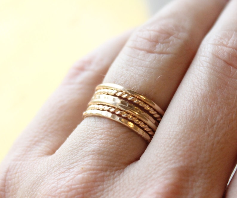 May include: A set of five gold stacking rings with different textures, including a twisted rope design and a hammered finish.