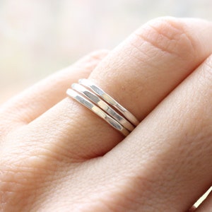 May include: Three silver hammered stacking rings worn on a finger.