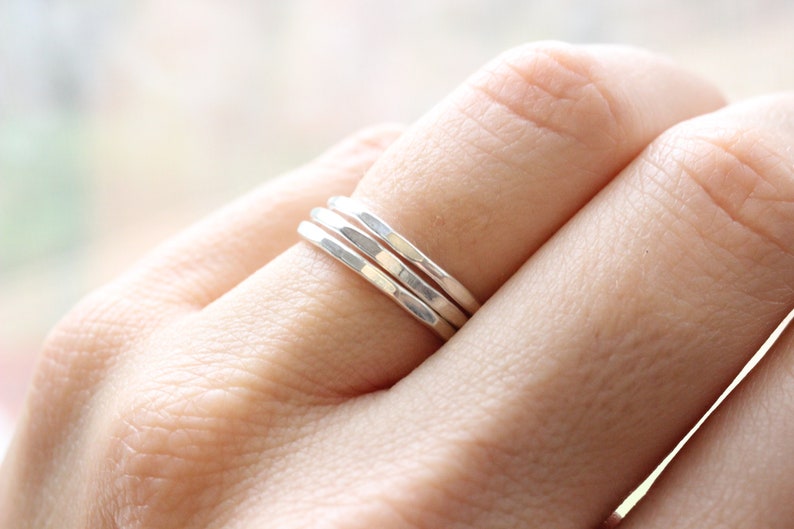 May include: Three silver hammered stacking rings worn on a finger.