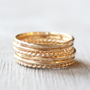 May include: A set of five gold stacking rings. The rings are all different styles, including hammered, twisted, and plain. The rings are stacked on top of each other, creating a unique and stylish look.