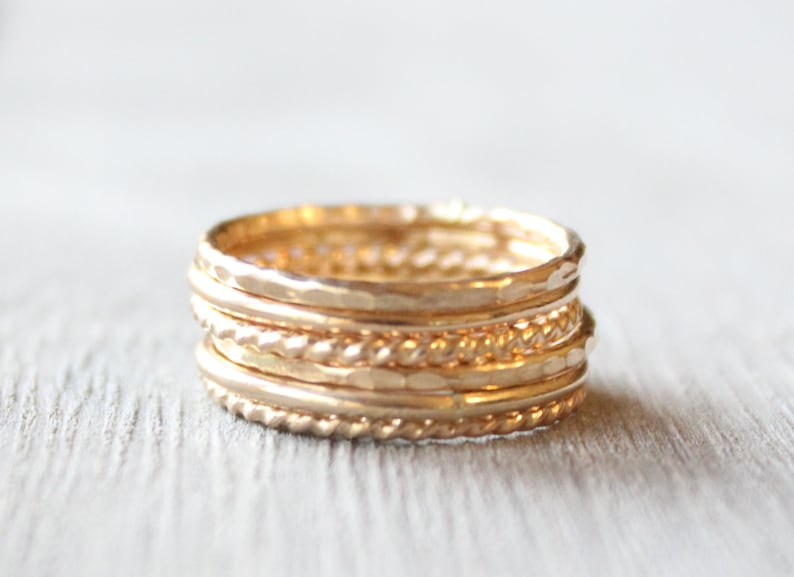 May include: A set of five gold stacking rings. The rings are all different styles, including hammered, twisted, and plain. The rings are stacked on top of each other, creating a unique and stylish look.