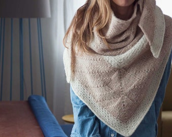 May include: A triangular shawl with a beige and white color gradient. The shawl is knitted with a delicate stitch pattern and has a fringed edge.