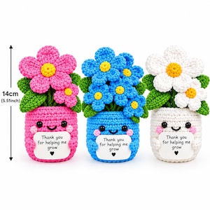 以下が含まれることがあります： ピンク、青、白の3つの編みぐるみの鉢植えの花で、高さはそれぞれ14cmです。鉢には笑顔が描かれており、'Thank you for helping me grow'という文字と黒いハートのアイコンが印刷された白い看板を持っています。