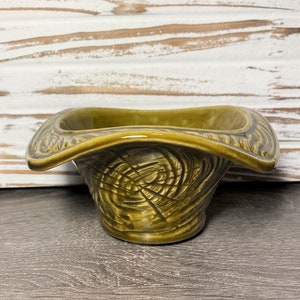 May include: A green ceramic bowl with a wide, flared rim and a swirling, textured design. The bowl is glazed and has a glossy finish.