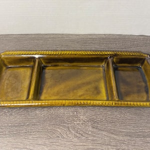May include: A brown ceramic serving dish with three divided sections. The dish has a textured rim.