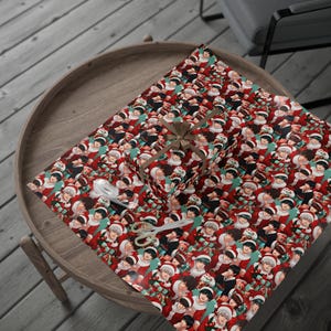May include: Wrapping paper featuring a repeating pattern of anime-style characters wearing red and white Santa Claus outfits against a teal background. A rectangular gift box is wrapped in the paper and tied with a brown ribbon.