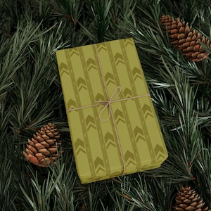 May include: A rectangular gift box wrapped in olive green paper featuring a repeating pattern of darker green chevron arrows and vertical dashed lines, secured with a thin, light brown twine tied in a simple bow across the center.