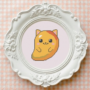 May include: A cross-stitch embroidery of a yellow, bean-shaped cat character with small ears, black eyes, and pink cheeks, displayed inside a round, ornate white frame with intricate floral carvings and a rope-textured inner border.