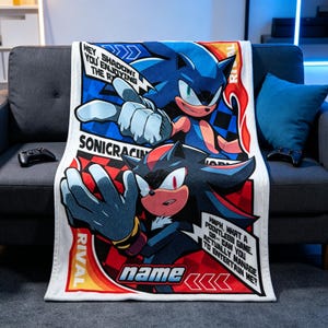 May include: A rectangular fleece blanket featuring a graphic print of Sonic the Hedgehog and Shadow the Hedgehog. The design includes comic-style speech bubbles with text, a checkered background, and the word name at the bottom in a bold font.