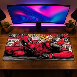 May include: A rectangular desk mat featuring a comic book graphic of the character Deadpool in a red and black suit. The design includes various comic panels with speech bubbles and sound effect text in the background, set against a dark surface.