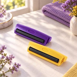 May include: Two handheld lint rollers with a compact design. One roller features a vibrant purple plastic casing, while the other has a bright yellow plastic casing. Both tools include a black adhesive roller surface for picking up debris.