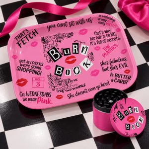 May include: A rectangular pink rolling tray and a matching cylindrical herb grinder. Both items feature the text Burn Book, red lip prints, and various quotes from the movie Mean Girls, including That's Fetch and On Wednesdays we wear Pink.