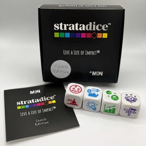 May include: A black box labeled stratadice Live a Life of Impact Coach Edition with a row of four white dice featuring colorful icons. Next to the box is a square black instruction card with the same branding and text in white and color.
