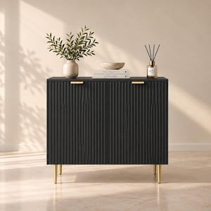 Op de afbeelding: Een zwarte rechthoekige opbergkast met verticaal geribbelde deurpanelen, twee horizontale goudkleurige metalen handgrepen en vier slanke goudkleurige metalen poten. Bovenop staan een beige vaas met bladeren, een stenen kom, twee boeken en een geurstokjeshouder.