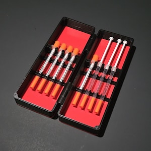 May include: A black plastic hinged case with a bright red interior lining, containing eight clear plastic syringes with orange caps. Each syringe features black measurement markings and the text Easy-Touch printed on the barrel.