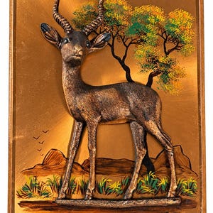 May include: A rectangular wall plaque featuring a three-dimensional bronze-toned gazelle sculpture mounted on a metallic gold background. The scene includes painted trees with yellow and green foliage, distant brown hills, and the signature Crastone.