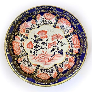 May include: Round decorative tray with a blue border and a floral design. The tray features a central cream-colored section with red and black floral patterns. The outer edge has a gold trim.