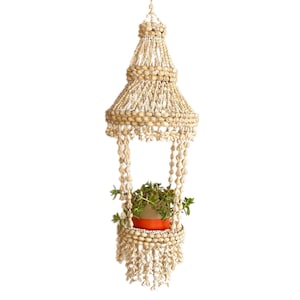 May include: A white hanging planter made of shells and beads with a small potted plant inside.