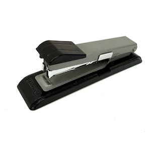 May include: A gray and black stapler on a white background. The stapler has a black base and top, with a gray body. The brand name "SOBITION" is printed on the base. A common office supply.