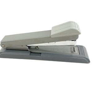 May include: A gray metal stapler with a white plastic top. The stapler is sitting on a gray base with the word "BOSTITCH" printed on the side.