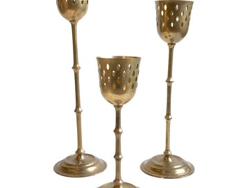 Puede incluir: Conjunto de tres candelabros de metal dorado con un diseño único. Cada candelero presenta una base redonda, un tallo alto y delgado y una copa decorativa con detalles recortados.