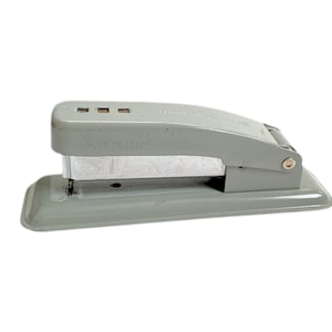 May include: A gray stapler with the text "Swingline CUB" and "LIFT TO LOAD" printed on it. The stapler is made of metal and has a rectangular base. The stapler is on a white background.