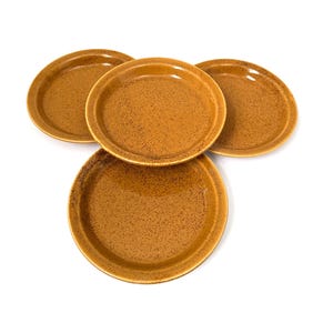 May include: Four round, speckled, brown plates are arranged on a white background. The plates have a slightly raised rim and a textured surface. The plates are a warm, earthy tone, suitable for serving food.