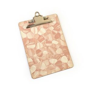 May include: A pink and white clipboard with a metal clip. The clipboard has a pattern of small, rounded shapes.