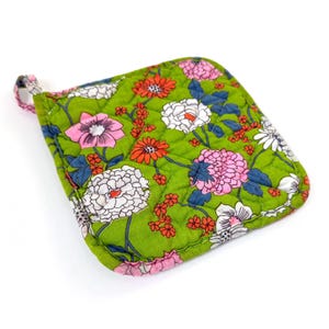 May include: A quilted, square-shaped pot holder with a green background and a floral pattern featuring pink, white, and orange flowers. The pot holder has a small loop for hanging and is designed for kitchen use.