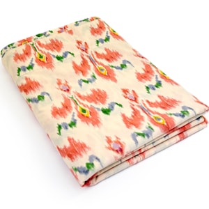 May include: Folded fabric with a cream background and a repeating pattern of red, yellow, green, and blue floral shapes. The fabric is folded neatly, showcasing the design and texture. The overall aesthetic is vibrant and decorative.