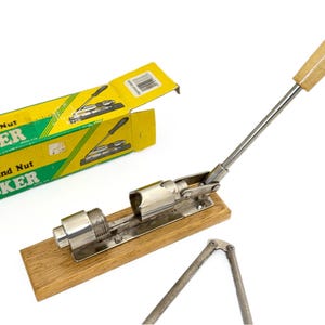 May include: A vintage pecan and nut cracker with a wooden handle and base. The metal cracker is attached to a wooden base and has a long lever. The box is yellow and green with the words "Pecan and Nut Cracker".