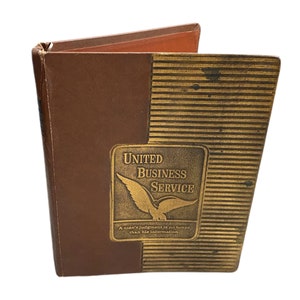 May include: A brown leather-bound book with gold lettering on the cover. The title is "United Business Service" and the cover has a gold eagle design. The text below the eagle reads "A man's judgment is no better than his information."