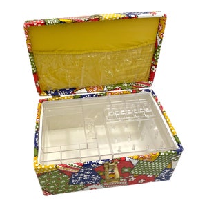 May include: A vintage sewing box with a colorful patchwork design. The box has a clear plastic insert with compartments for needles, thread, and other sewing supplies.