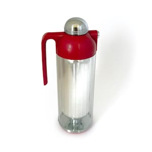 May include: A vintage red and silver thermos with a handle and a chrome lid. The thermos has a cylindrical shape and a red handle. The top of the thermos is red, and the lid is chrome.