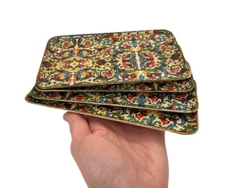 May include: Set of four vintage decorative trays with a colorful floral pattern. The trays are made of a hard, lightweight material and have a gold trim.