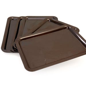 May include: A stack of rectangular brown trays with slightly raised edges. The trays are made of a glossy material and are arranged in a slightly fanned-out pattern, showcasing their shape and color. The trays are suitable for serving food.