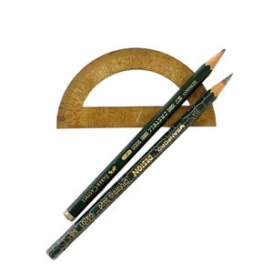 May include: A brass protractor with a black and gold pencil and a green and gold pencil. The pencils are labeled "DESIGN DRAWING 9001" and "FABER-CASTELL 771611-CS7877 GERMANY".