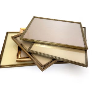 May include: A collection of rectangular picture frames with ornate gold and bronze-colored borders. The frames are stacked, revealing the glass and backing. The background is white.