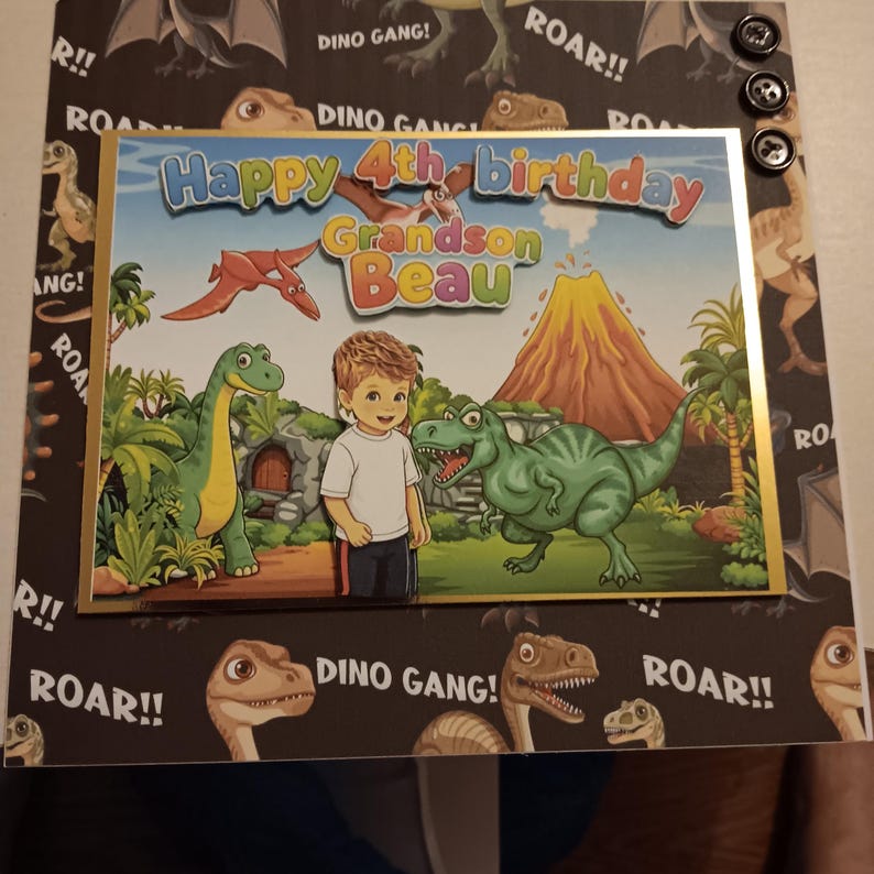May include: A birthday card featuring a cartoon illustration of a child standing between a green long-necked dinosaur and a green T-Rex in a prehistoric landscape with a volcano. The text reads Happy 4th birthday Grandson Beau.
